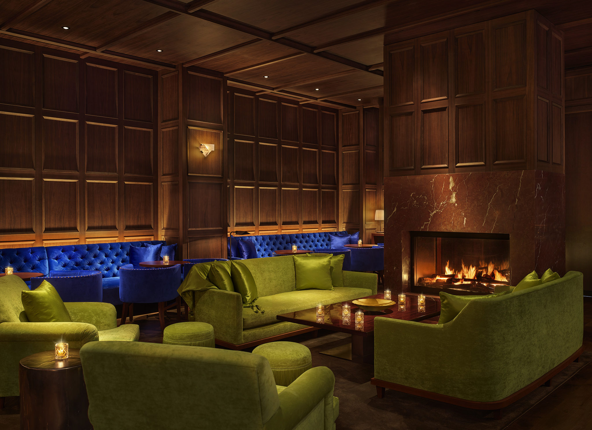 Dimly lit lounge with bright blue and green velvet seating and fireplace
